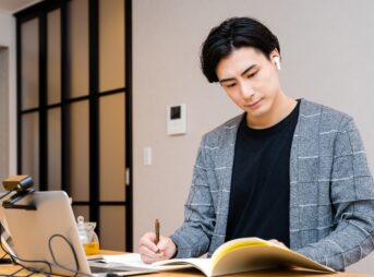 オンライン英会話のレッスンを受けながら自宅で勉強する男性