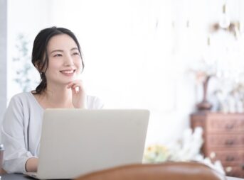 ノートパソコンの前で考える笑顔の女性
