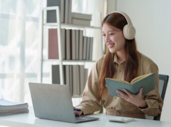本を片手にノートパソコンを操作する女性
