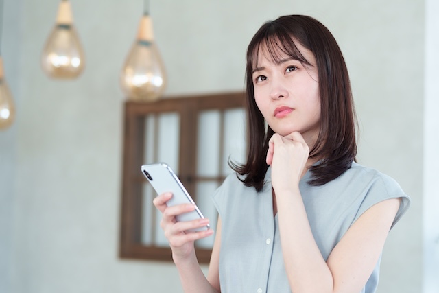 スマホを持ちながら考える女性