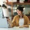 カフェでパソコンを見ながら勉強するヘッドセットを首にかけた女性