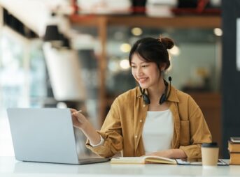 カフェでパソコンを見ながら勉強するヘッドセットを首にかけた女性