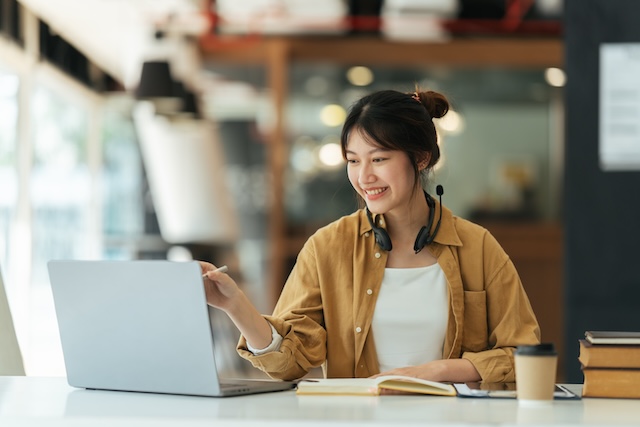 カフェでパソコンを見ながら勉強するヘッドセットを首にかけた女性