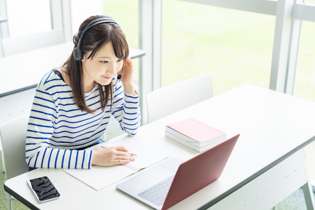教室でオンライン英会話のレッスンを受ける私服の若い女性