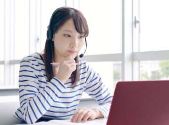 教室でオンライン英会話レッスンを受けながら考える若い女性