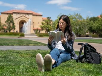 海外の大学の敷地内で本を読む女子大学生
