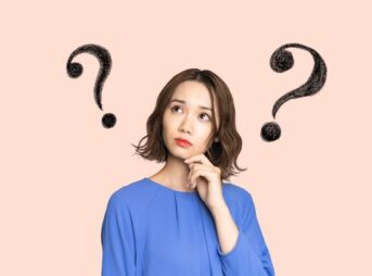 はてなマークが浮かぶ青い服を着た日本人女性