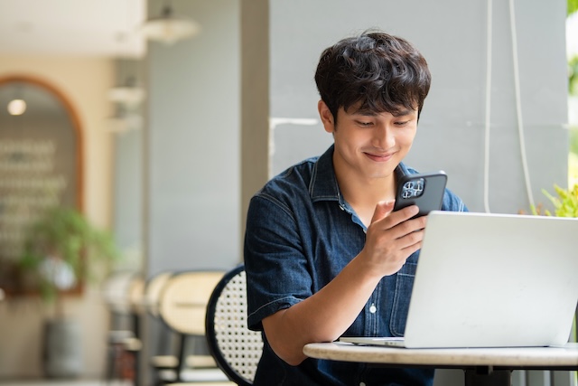 カフェでスマートフォンを見ながら喜ぶ男性