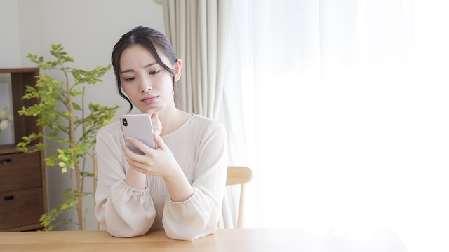 眉間にシワを寄せてスマートフォンを見る女性