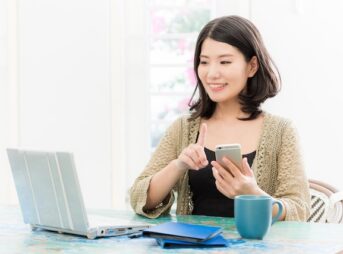 ノートパソコンを見ながらスマートフォンで申し込む女性